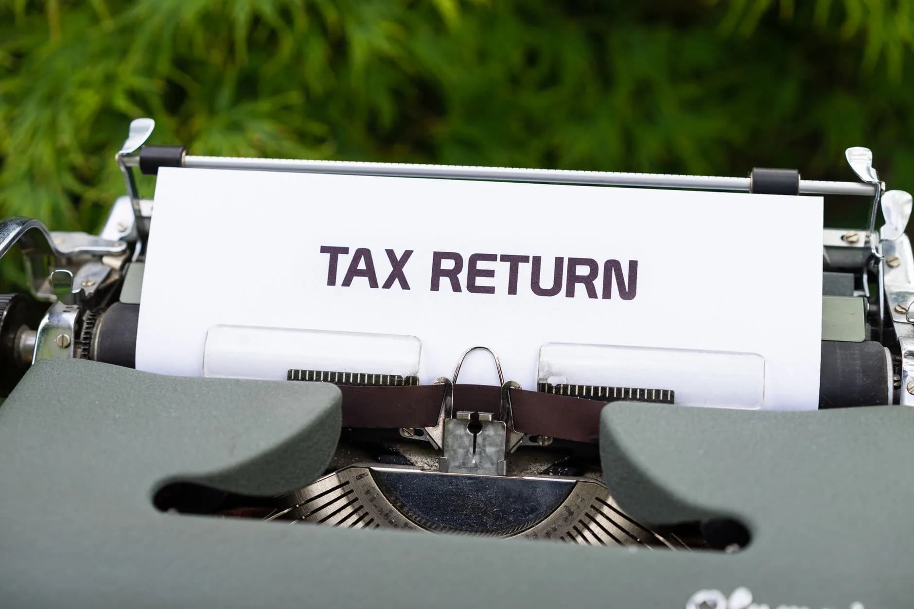 Close-up of a vintage typewriter typing 'Tax Return' on paper outdoors.