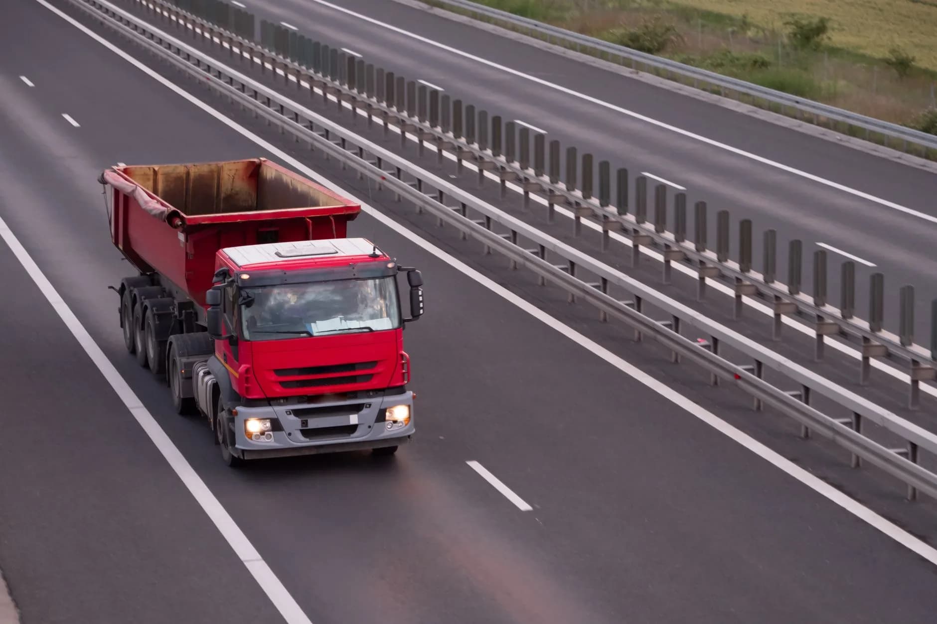 An overhead view of a red dump truck driving on an open highway during the day.
