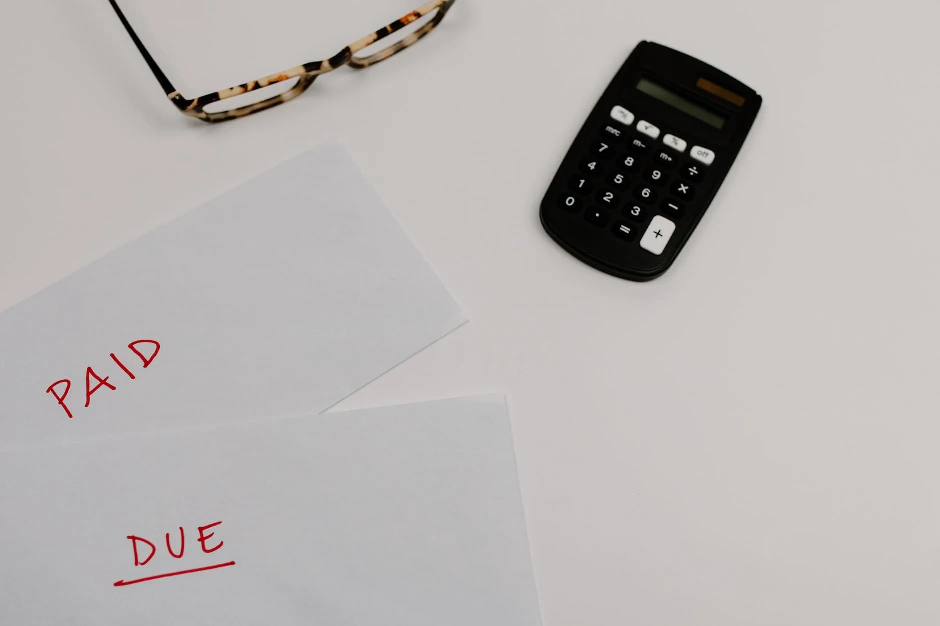 Top view of financial papers labeled 'Paid' and 'Due' beside a calculator and glasses.