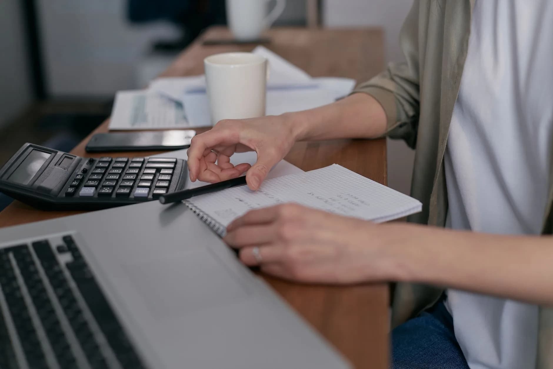 A mid-adult calculating finances with a laptop and notepad, managing budgets at home.