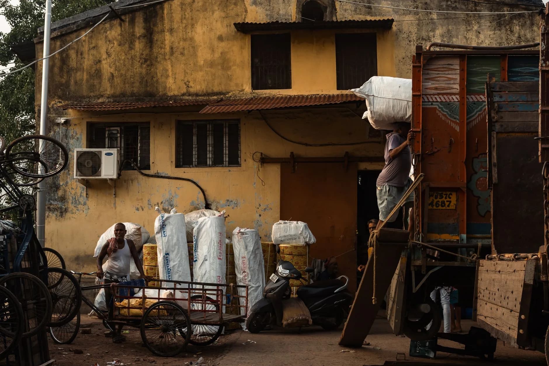 Workers unloading goods from a truck in a rustic setting in Kolkata, India.